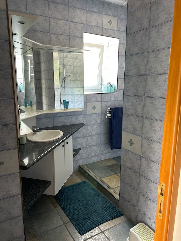 Salle de bain carrelée de bleu avec douche et meuble vasque